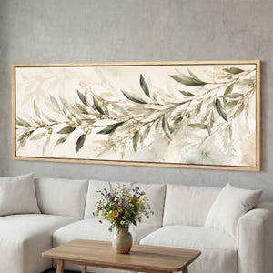 Könnte beinhalten: Ein rechteckiger Leinwandkunstdruck mit einem Aquarelldesign von Olivenzweigen mit grünen und olivfarbenen Blättern. Das Kunstwerk ist in einem hellen Holzrahmen gerahmt und hängt über einem weißen Sofa.