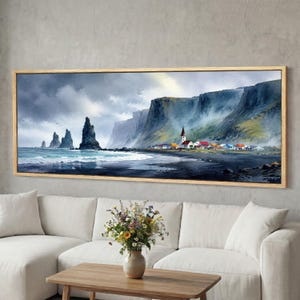 May include: A framed watercolour painting of a coastal scene with towering cliffs, a black sand beach, and a village. The artwork shows a dramatic sky, dark rock formations, and a wooden frame. The painting is displayed above a white sofa.