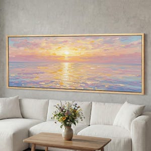 Pode incluir: Uma pintura a óleo emoldurada retrata um pôr do sol sobre o oceano. A obra de arte apresenta uma paleta de tons rosa, amarelo e azul, com o reflexo do sol na água. A pintura está pendurada acima de um sofá branco e de uma mesa de centro de madeira.