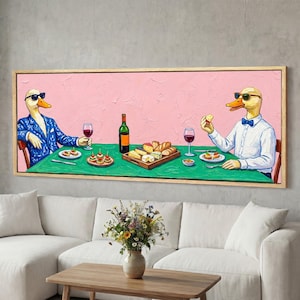 May include: A framed painting depicts two anthropomorphic ducks dining at a table. One duck wears a blue suit, the other a white shirt and bow tie. The table is set with food, wine, and a bottle against a pink background.