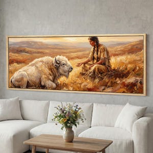 May include: A framed painting depicts a Native American woman seated in a field, interacting with a white bison. The artwork is rendered in warm, earthy tones, with a focus on the connection between the woman and the animal. The painting is displayed above a white sofa.