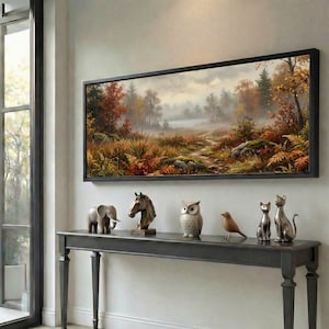 May include: A framed landscape painting of an autumnal forest scene with a path to a lake. Below, a dark grey console table displays decorative animal figurines: an elephant, horse head, owl, bird, and two cats.
