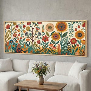Puede incluir: Una impresión floral enmarcada con una vibrante variedad de flores estilizadas en tonos de rojo, naranja, amarillo y azul sobre un fondo crema. La obra de arte está encerrada en un marco de madera marrón claro, creando una decoración de pared.