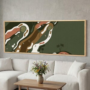 May include: A framed art print depicting a golf course scene. The artwork features a stylized landscape with golfers, palm trees, and a color palette of greens, browns, and white. The rectangular frame is made of light-colored wood.
