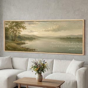 Op de afbeelding: Een ingelijste landschapsafdruk met een serene meer, een boom aan de linkerkant en bergen in de verte. Het kunstwerk heeft een vintage esthetiek met zachte kleuren en bevat de tekst "Blessed is the one who trusts in the Lord. They will be like a tree planted by the water. Jeremiah 17:7-8."