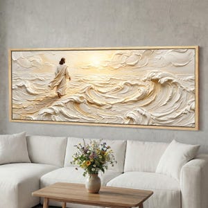 Puede incluir: Una obra de arte texturizada enmarcada representa una figura caminando sobre el agua hacia una luz dorada brillante. La pintura en relieve presenta una paleta de colores neutros y un marco de madera marrón claro. La obra está sobre un sofá blanco.