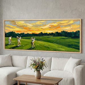 May include: An oil painting of a golf course scene with three golfers in action. The artwork features a vibrant sunset with yellow and orange hues, set above a green golf course and dark green trees. The painting is framed in a light wood frame.