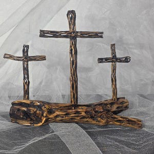 May include: A decorative display featuring three crosses crafted from dark brown, porous cholla wood. The crosses are mounted upright on a horizontal, textured log base of the same material, showcasing natural hollows and a rugged, organic surface.