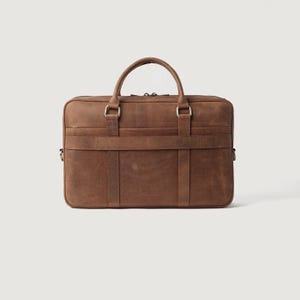 May include: A brown leather briefcase with a top handle and a shoulder strap. The briefcase has a rectangular shape with a flap closure and metal hardware. The leather has a distressed look.