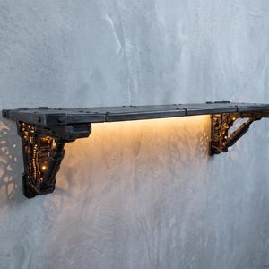 May include: A dark grey, industrial-style wall shelf with integrated lighting. The rectangular shelf has visible rivets and a textured surface. The supports feature intricate, mechanical designs. Warm light illuminates the shelf's underside, creating a dramatic effect.