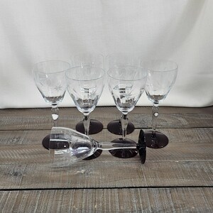 May include: A set of six clear glass wine glasses with deep purple stems and bases. Each glass features a delicate etched starburst pattern on the bowl. Five glasses stand upright in two rows, while one glass lies horizontally in the foreground.