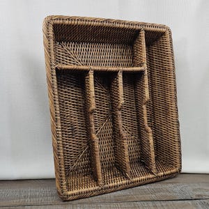 May include: A rectangular brown woven rattan cutlery tray featuring five distinct compartments. The organizer is constructed with a tight, intricate weave pattern and includes one horizontal section at the top and four vertical sections below.