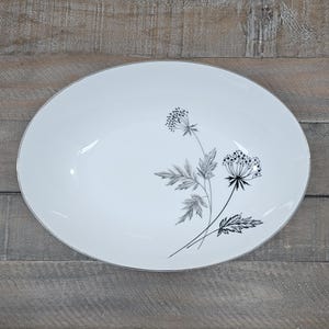 May include: A white ceramic mug with a black handle and the text "But First, Coffee" in a black, handwritten-style font. The mug is on a white surface.