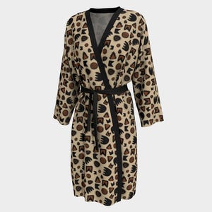 May include: A beige dressing gown featuring a repeating pattern of brown and black abstract shapes. The gown has black trim and a matching belt. The garment is made of a soft, flowing fabric.