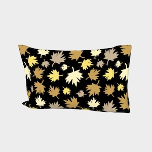 May include: A rectangular pillow with a black background and a repeating pattern of stylized maple leaves in shades of gold, tan, and cream. The pillow is a decorative item, likely for a bed or sofa.