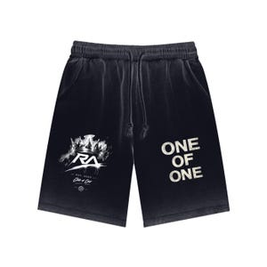 May include: Black shorts with a drawstring waist and a faded look. The left leg has a white graphic of a crown and the letters "RA". The right leg displays the text "ONE OF ONE" in a distressed font.