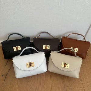 Könnte beinhalten: Fünf kleine, strukturierte Handtaschen mit genarbter Textur, jeweils mit einem Tragegriff und einem goldfarbenen Drehverschluss mit Bambus-Akzent. Die Kollektion umfasst Taschen in den Farben Schwarz, Dunkelbraun, Hellbraun, Weiß und Creme.