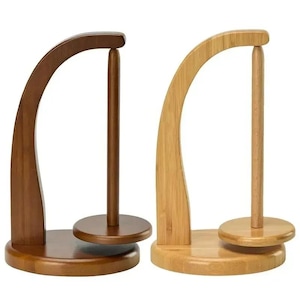 May include: Two wooden paper towel holders. One is a dark brown color, and the other is a light tan color. Each has a curved arch and a central dowel for holding paper towels. The base is a round, flat disc.