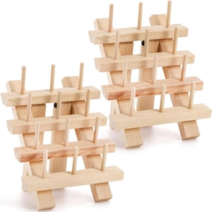 May include: Two wooden thread spool holders. Each holder is constructed with multiple horizontal wooden planks supported by vertical wooden posts. The holders have several vertical pegs for holding spools of thread. The wood has a natural, light color.