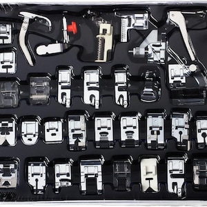 May include: A set of sewing machine presser feet in a black plastic organizer. The set includes various silver-colored feet for different sewing techniques, such as zippers, buttonholes, and decorative stitches. The organizer is sealed in clear plastic.