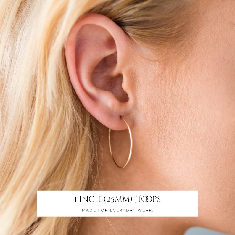 Puede incluir: Un pendiente de aro fino de oro con un dise&ntilde;o de alambre circular. El texto en la imagen dice 1 INCH (25MM) HOOPS MADE FOR EVERYDAY WEAR. El pendiente es un anillo de metal pulido sencillo que atraviesa el l&oacute;bulo de la oreja.