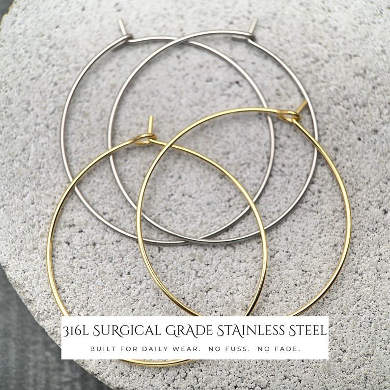 Puede incluir: Dos pares de pendientes de aro finos, un par en metal plateado y otro en metal dorado. El texto superpuesto dice: 316L SURGICAL GRADE STAINLESS STEEL. BUILT FOR DAILY WEAR. NO FUSS. NO FADE. Estos pendientes circulares cuentan con un cierre de alambre.