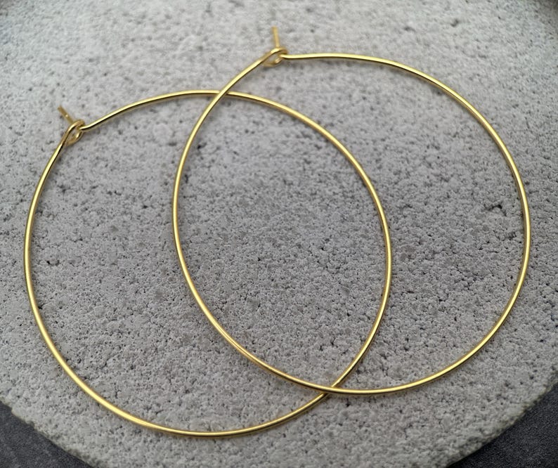 Puede incluir: Un par de pendientes de aro dorados, finos y circulares. Cada pendiente presenta un dise&ntilde;o de alambre simple y continuo con un peque&ntilde;o mecanismo de cierre integrado en la parte superior donde se unen los extremos, creando una silueta circular.