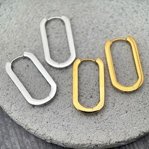 May include: A set of four hoop earrings featuring an elongated oval shape. Two of the earrings are finished in a polished silver tone, while the other two are finished in a polished gold tone. Each earring includes a hinged post closure.
