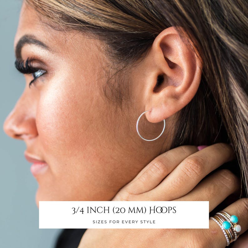 Puede incluir: Un pendiente de aro circular fino de plata usado en el l&oacute;bulo de la oreja. La imagen incluye el texto 3/4 INCH (20 MM) HOOPS SIZES FOR EVERY STYLE. El pendiente presenta un dise&ntilde;o de alambre simple con un acabado met&aacute;lico pulido y una forma circular.