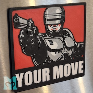 May include: A rectangular magnet featuring a stylized image of a cyborg holding a gun, set against a red background. The phrase "YOUR MOVE" is printed in white block letters below the image. The cyborg is primarily black and gray.