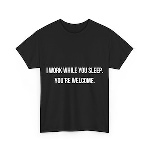 May include: Black t-shirt featuring the white text: "I WORK WHILE YOU SLEEP. YOU'RE WELCOME." The t-shirt has a crew neck design. The text is centrally positioned on the front of the garment, suitable for everyday wear.