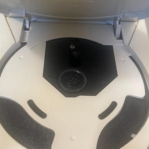 May include: An open, off-white vintage video game console with a black disc tray. The console's lid is raised, revealing the internal components. The design includes a circular disc tray and a dark gray foam pad.