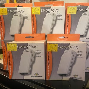Puede incluir: Múltiples cajas del accesorio "EMOR PAK" para la SEGA DREAMCAST. Cada caja presenta un dispositivo blanco con el texto "Feel Every Jolt, Bump And Blast With The TremorPak!" y el logotipo "PERFORMANCE".