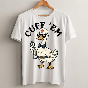 以下が含まれることがあります： サングラス、看護師の帽子、蝶ネクタイをつけた漫画のガチョウの上に「CUFF 'EM」という文字が書かれた白いTシャツ。ガチョウはストップウォッチを持っています。デザインは黒、赤、青、黄色のアクセントがあります。