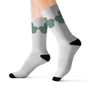 Puede incluir: Calcetines blancos con un diseño de trébol verde. Los calcetines tienen talones y punteras negras. El diseño del trébol está formado por líneas concéntricas, creando un efecto 3D. Los calcetines son acanalados.
