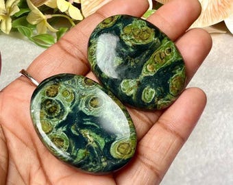 Puede incluir: Dos piedras preciosas ovaladas pulidas, con un color base verde oscuro y patrones intrincados de verde claro y marrón. Las piedras son lisas y reflectantes, mostrando variaciones naturales.