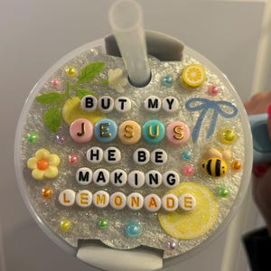 K&ouml;nnte beinhalten: Ein dekorativer Becherdeckel mit Strohhalm, mit dem Text "BUT MY JESUS HE BE MAKING LEMONADE", der mit bunten Buchstabenperlen geschrieben wurde. Der Deckel ist mit Zitronen- und Bienenverzierungen versehen.