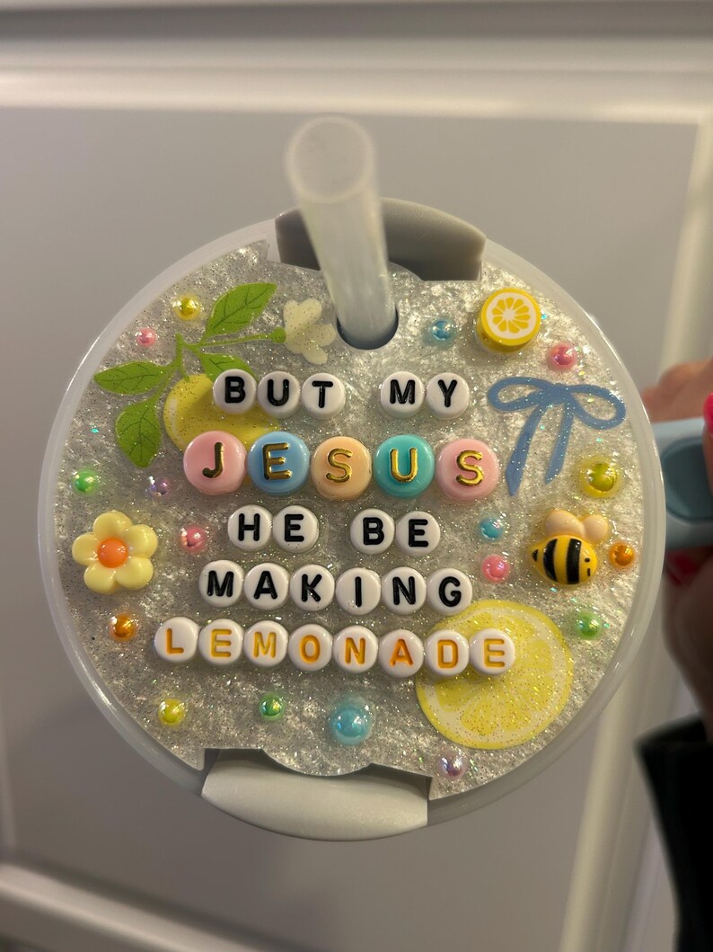 K&ouml;nnte beinhalten: Ein dekorativer Becherdeckel mit Strohhalm, mit dem Text "BUT MY JESUS HE BE MAKING LEMONADE", der mit bunten Buchstabenperlen geschrieben wurde. Der Deckel ist mit Zitronen- und Bienenverzierungen versehen.