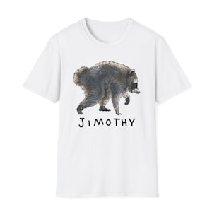 Pode incluir: Uma t-shirt branca de manga curta com uma ilustração em estilo aguarela de um guaxinim cinzento-escuro e preto a caminhar. Abaixo do guaxinim, o nome JIMOTHY está impresso em letras maiúsculas pretas simples desenhadas à mão.