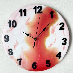 May include: Round wall clock with a white and red abstract design. Black numerals mark the hours. The clock hands are black. The clock is a decorative item for a home or office.