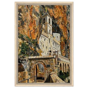 May include: A framed painting of a monastery built into a cliff face. The building is white with a bell tower and gold crosses. The surrounding rock face is a mix of orange and brown hues, with a stone archway in the foreground.