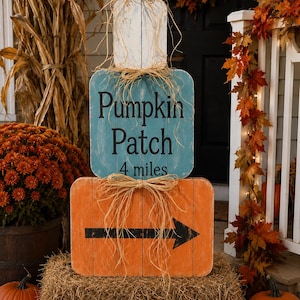 May include: A vertical wooden sign stack featuring three rectangular boards. The top is white, the middle is teal with the black text "Pumpkin Patch 4 miles," and the bottom is orange with a black arrow pointing right. Each board has a raffia bow.