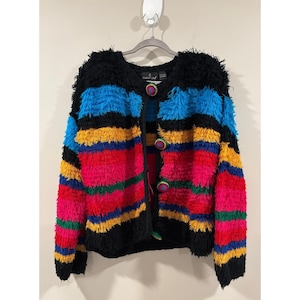 May include: A long-sleeve cardigan featuring a shaggy, textured knit with horizontal stripes in black, bright blue, yellow, hot pink, and green. The garment has a round neckline and is fastened with four large, round, multi-colored crochet buttons.