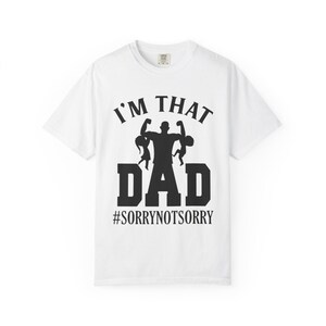 Può includere: T-shirt bianca con grafica nera che recita "I'M THAT DAD" con la silhouette di un uomo che tiene due bambini. Sotto la parola "DAD" c'è l'hashtag "#SORRYNOTSORRY".