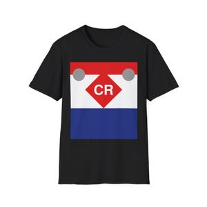 Puede incluir: Camiseta negra con un diseño gráfico. El diseño presenta un patrón de bloques de color rojo, blanco y azul. El diseño incluye las letras "CR" en forma de rombo rojo, con dos círculos grises en la parte superior.