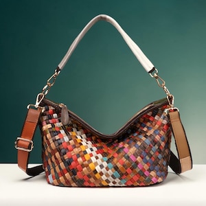May include: A colorful woven leather shoulder bag with a white top handle and a brown adjustable strap. The bag features a zipper closure and gold-tone hardware. The woven pattern incorporates various colors, including red, blue, yellow, and brown.