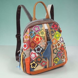 May include: A multi-colored leather backpack featuring a diamond-patterned patchwork design. The exterior is adorned with numerous small, three-dimensional leather flower appliqués in various colors. It includes a top handle, adjustable straps, and a central vertical zipper closure with a blue leather pull tab.