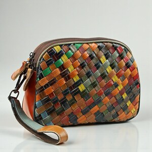 Puede incluir: Un bolso de mano de cuero tejido multicolor con forma redondeada. El bolso presenta una variedad de colores, incluyendo naranja, verde, amarillo y azul. Tiene una cremallera marrón y una correa de muñeca. El bolso mide aproximadamente 23 cm de ancho.