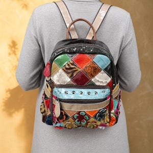 May include: A multi-colored backpack featuring a patchwork design with various textures, including faux snakeskin and animal print patterns. The bag includes a front zippered pocket with silver studs, a top handle, and floral-shaped embellishments.