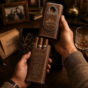 Peut inclure: Un étui à cigares en cuir marron avec un coupe-cigare en métal, gravé du nom TIMOTHY et d'un motif de montagne. L'étui porte le texte To the BEST DAD, A father's love is like a mountain, strong, steady, and always there to guide me.